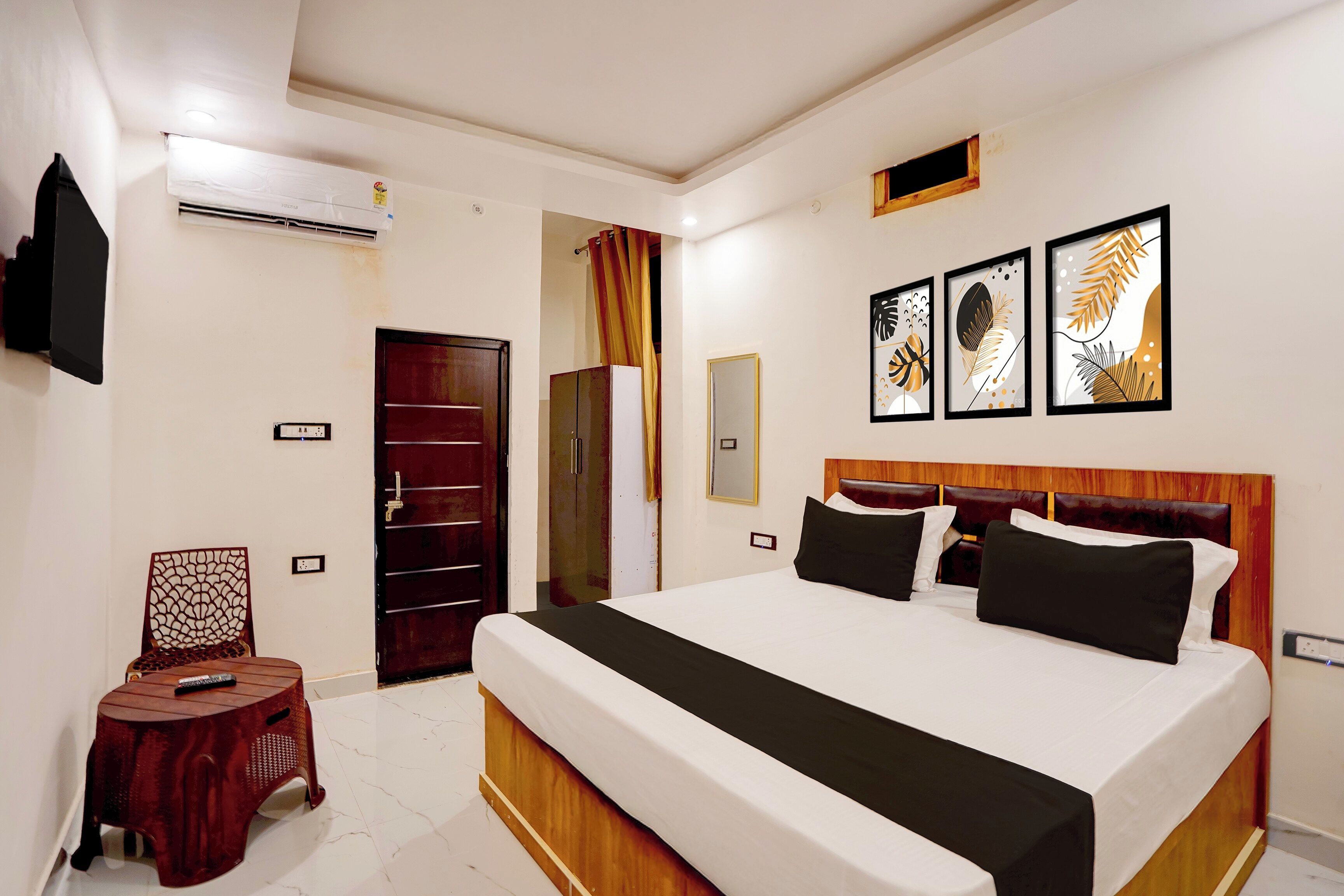 A hotel room with a large bed, a TV, a wardrobe, and a small stool.
