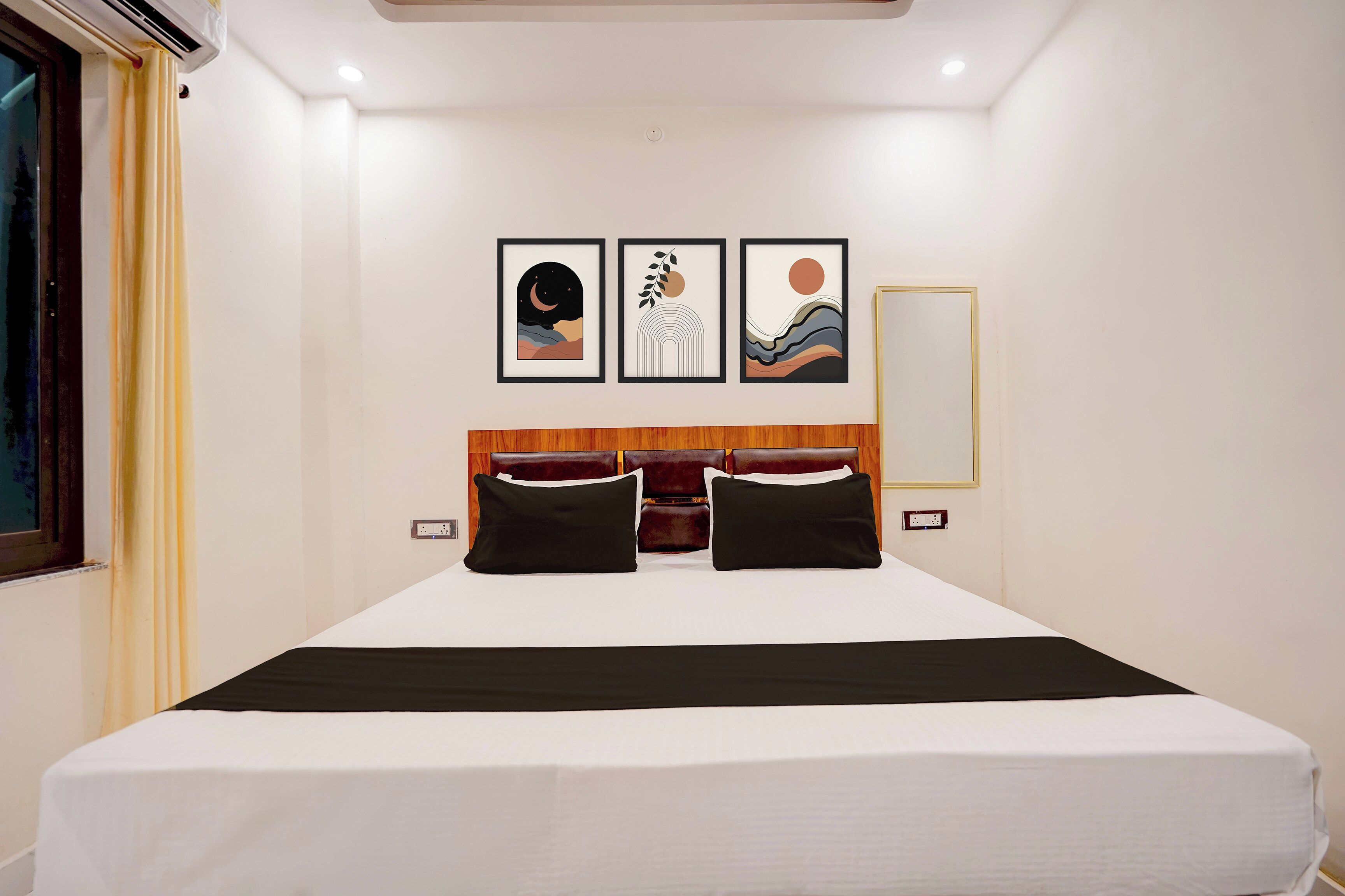 A hotel room with a large bed, a headboard with a wooden panel, and three framed artworks on the wall.