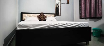 Una cama con cabecera, un almohadón y un cesto de basura verde.