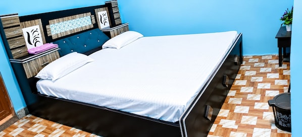A bed with a white mattress and a dark headboard, a wooden nightstand with a pink towel, and a potted plant on a blue wall. - Hotel O Sankar Hotel and Restaurant (Bara)