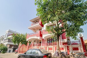 A multi-story residential building with a red and white facade, a gated entrance, and a tree in front. - Hotel O Raka Inn (Prayagraj)
