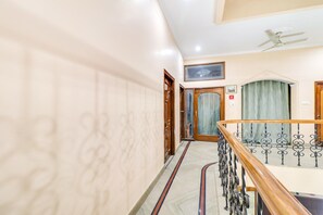 A hotel corridor with a marble floor, wooden doors, a ceiling fan, and a staircase with a metal railing. - Hotel O Raka Inn (Prayagraj)