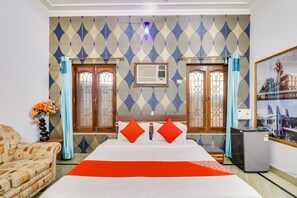 A hotel room with a large bed, two doors, a wall-mounted air conditioner, a small table with a vase of flowers, and a framed picture on the wall. - Hotel O Raka Inn (Prayagraj)