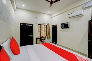 A hotel room with a bed, a chair, a TV, an air conditioning unit, and a ceiling fan. - Hotel O The Raghav Villa (Prayagraj)