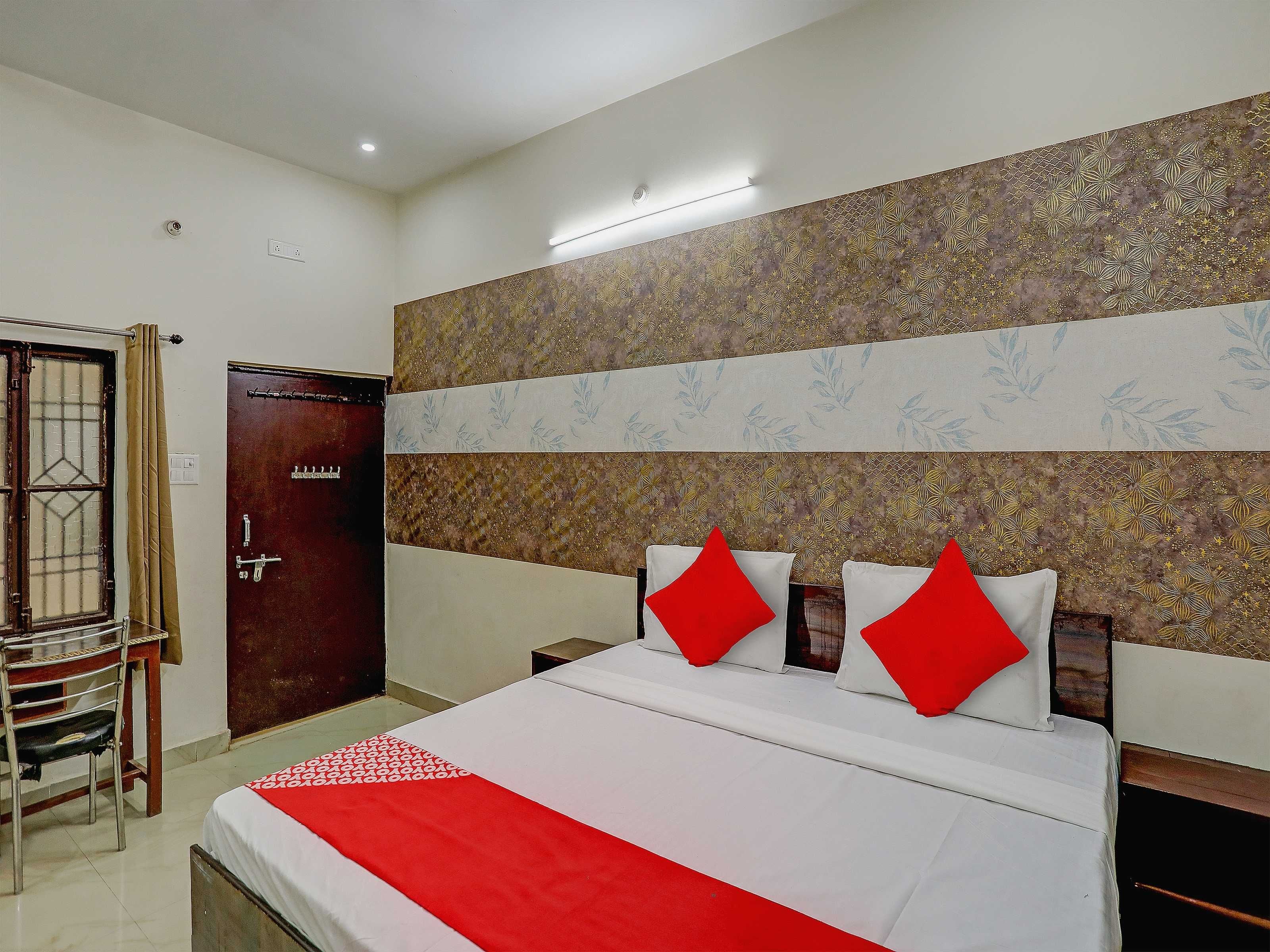 A hotel room with a bed, a wooden door, a chair, and a patterned wall.