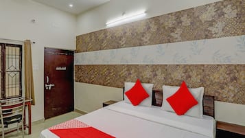 A hotel room with a bed, a wooden door, a chair, and a patterned wall.