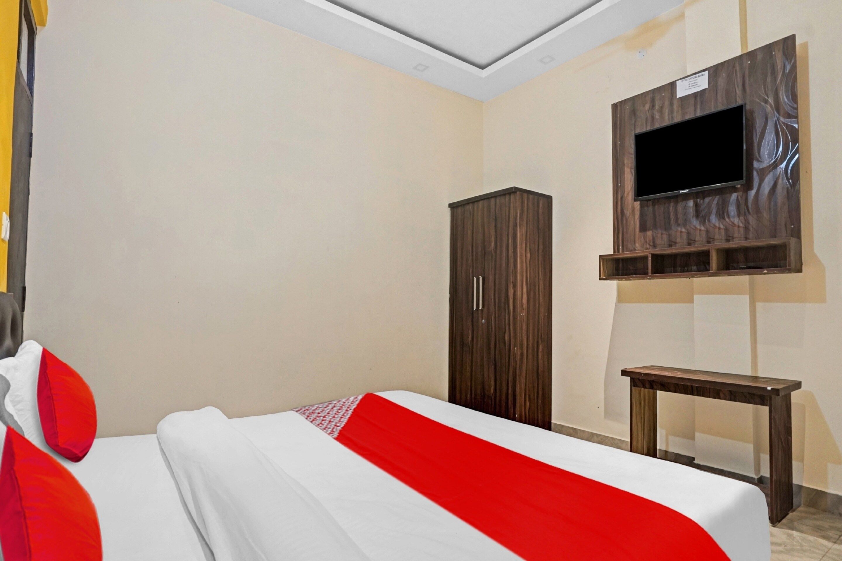 A hotel room with a bed, a wardrobe, a TV mounted on the wall, and a small table.