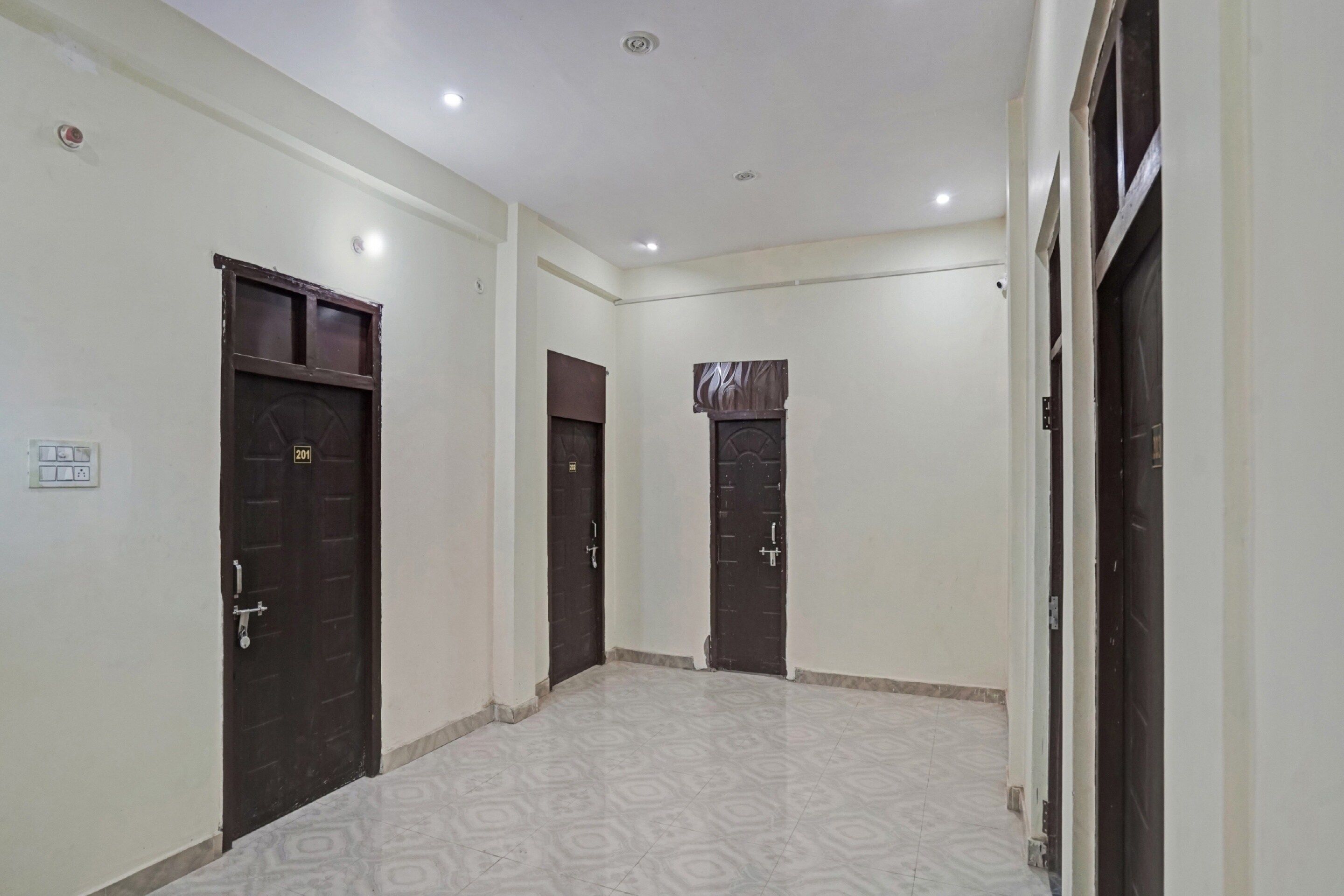 Un pasillo con tres puertas de madera oscura, paredes blancas y baldosas de suelo con diseño.