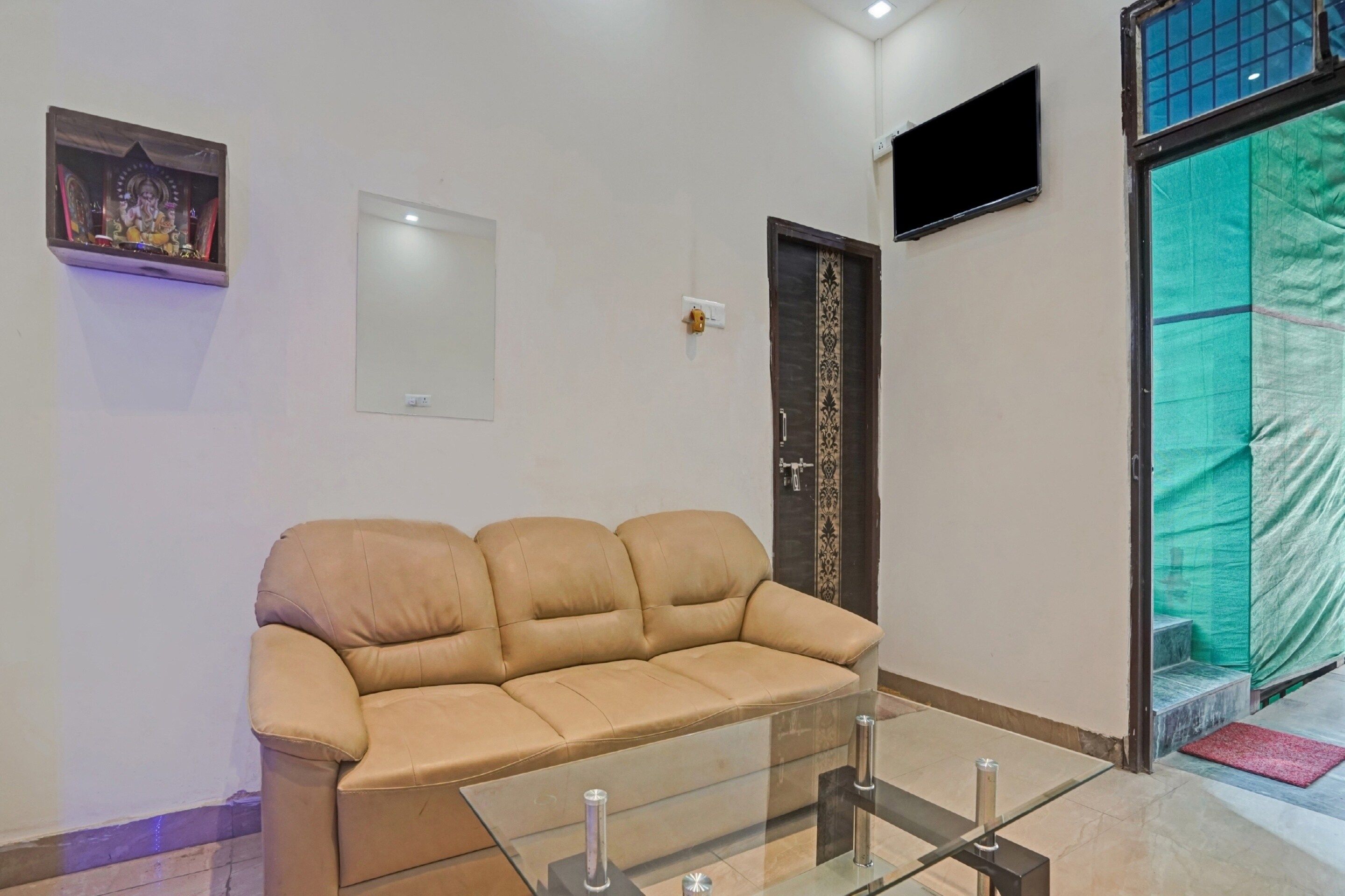 A beige sofa in a room with a glass coffee table, a wall-mounted TV, and a door with a decorative pattern.