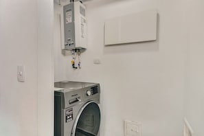 A laundry room with a front-loading washing machine and a water heater mounted on the wall. - New Listing (Bogotá)
