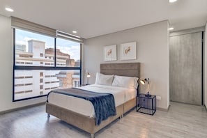 A modern bedroom with a large window, a bed, bedside tables, and artwork on the wall. - New Listing (Bogotá)