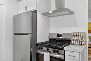 A modern kitchen with stainless steel appliances, including a refrigerator, oven, and stove, with a built-in spice rack. - The Velvet Cactus, Private Pool, Fire Pit, BBQ, & King Bed (Indio)