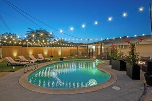 Une piscine avec des chaises longues et des guirlandes lumineuses.