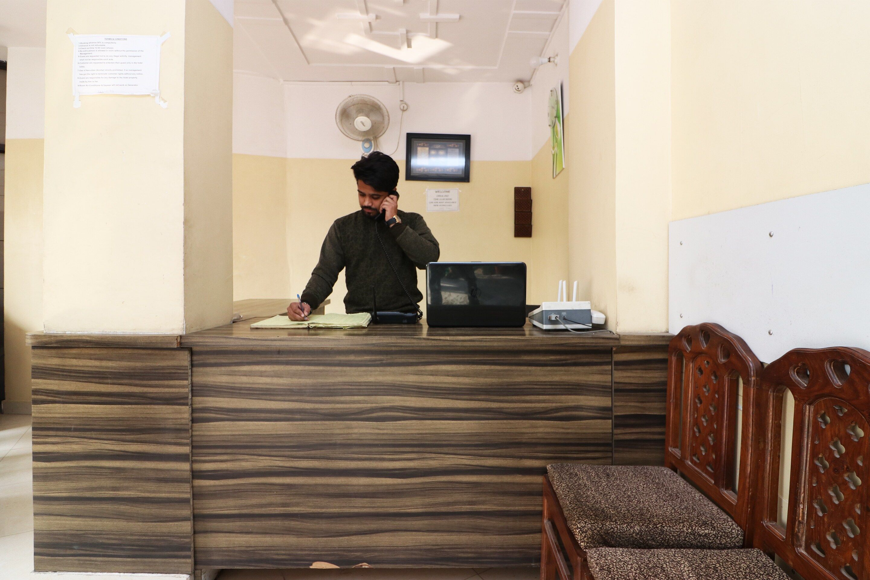 A reception desk with a person writing, a fan, and a clock on the wall.