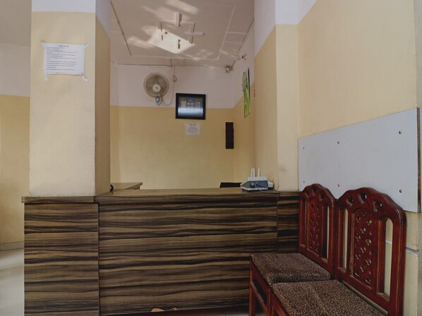 A reception area with a wooden reception desk, a bench, a wall-mounted fan, and a whiteboard.