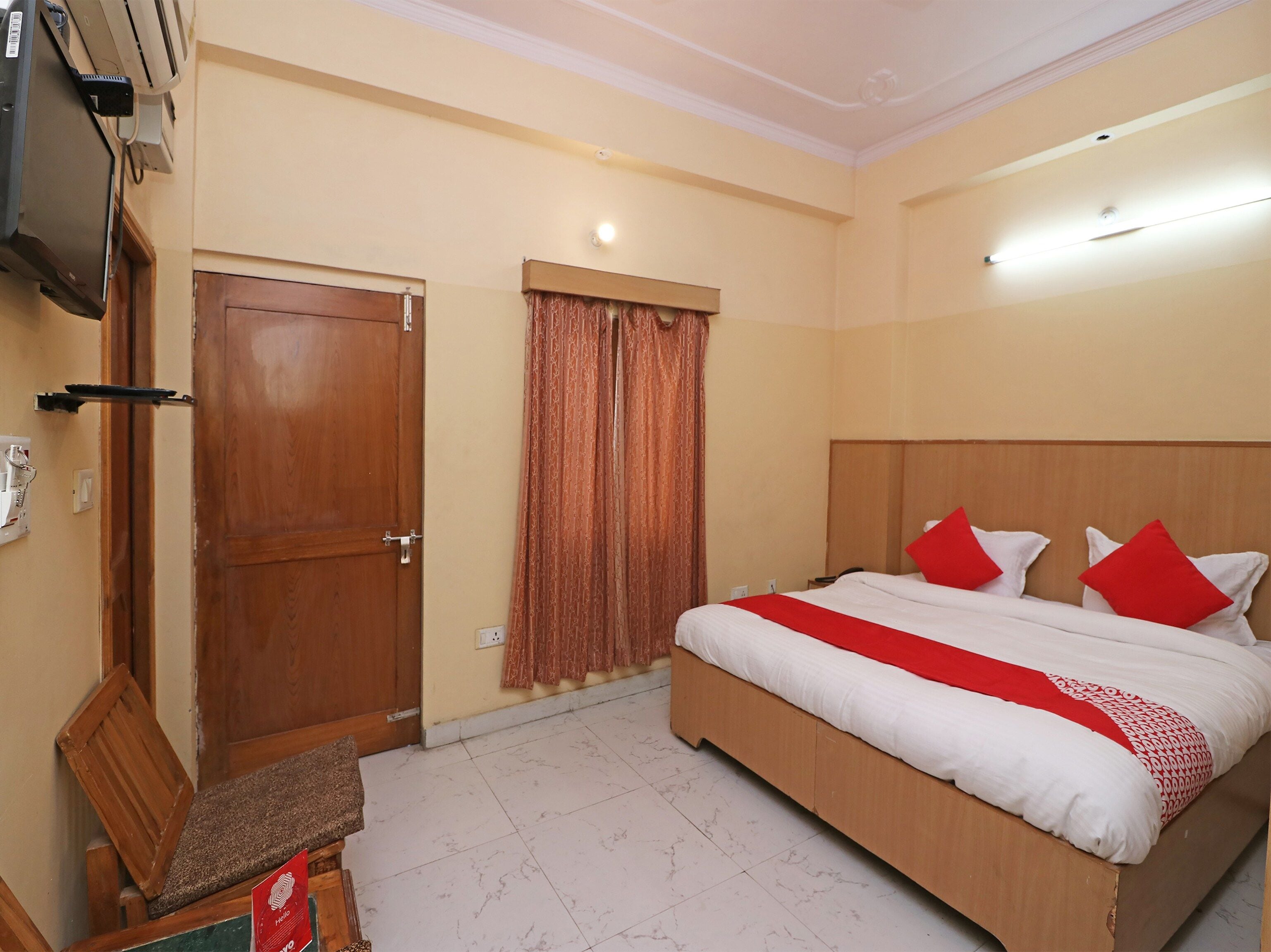 A hotel room with a bed, a television, a door, and a window with curtains.