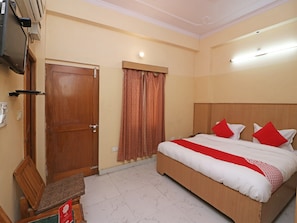 A hotel room with a bed, a television, a door, and a window with curtains.