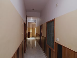 A corridor with wooden paneling on the walls and a tiled floor, leading to a room with a window and a door.