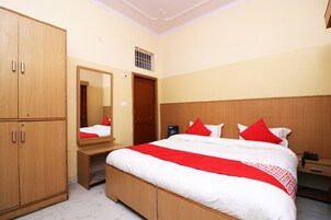 Una habitación de hotel con cama, armario, espejo, mesita de noche y velador.