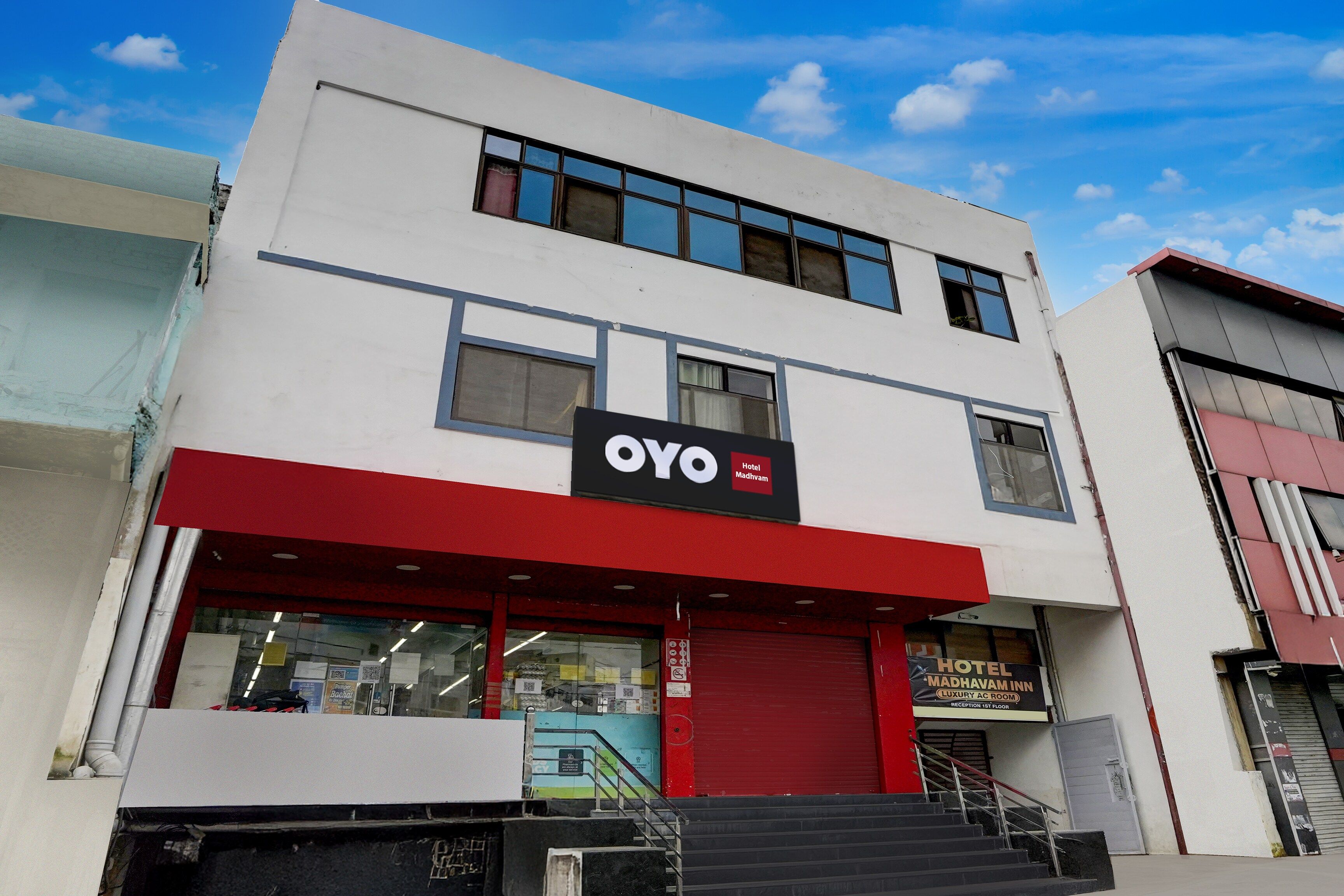 Un hotel con toldo rojo, un letrero que dice 'OYO Hotel Madhavam' y una escalera que lleva a la entrada.