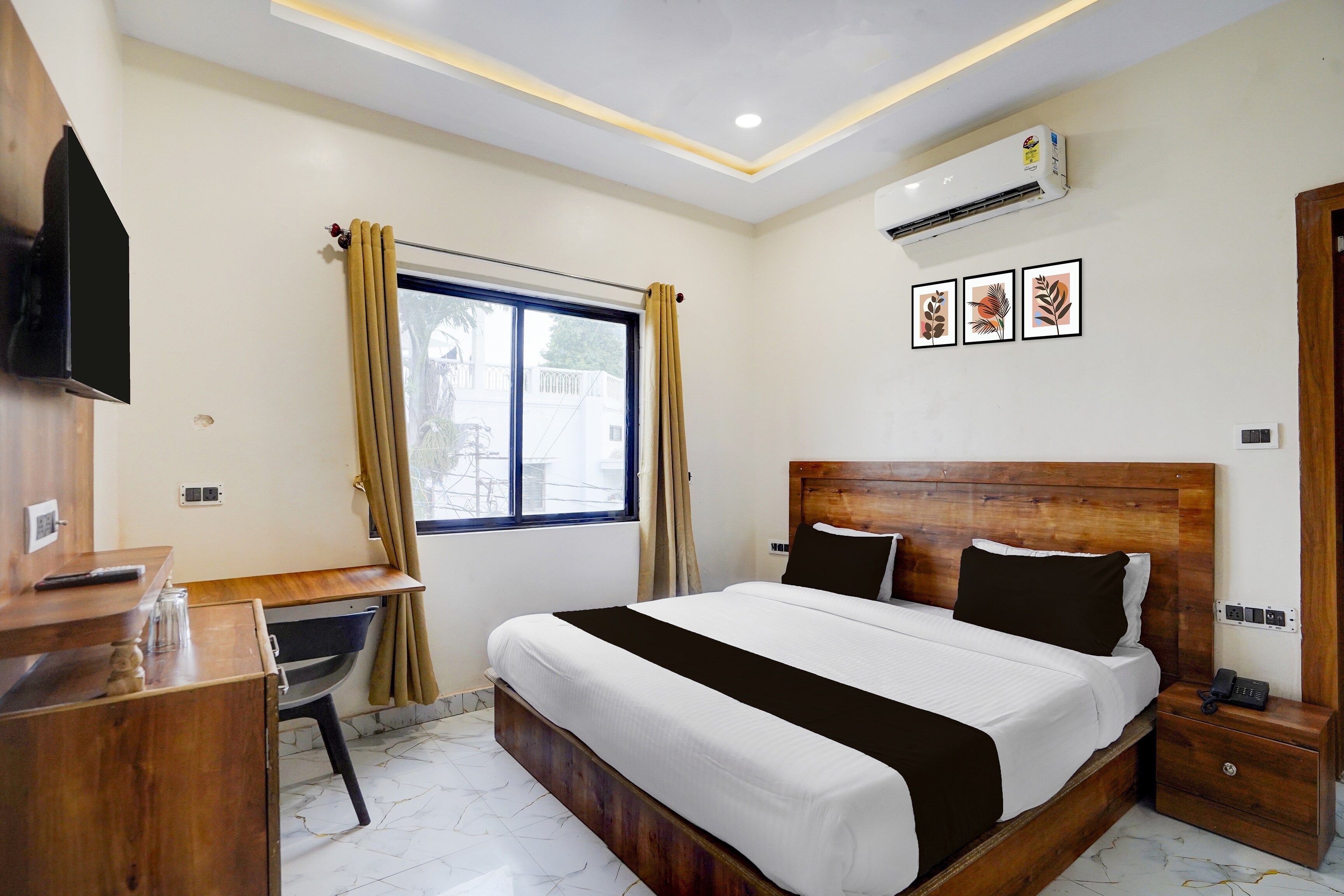 A hotel room with a bed, a desk, a chair, a TV, and an air conditioning unit.
