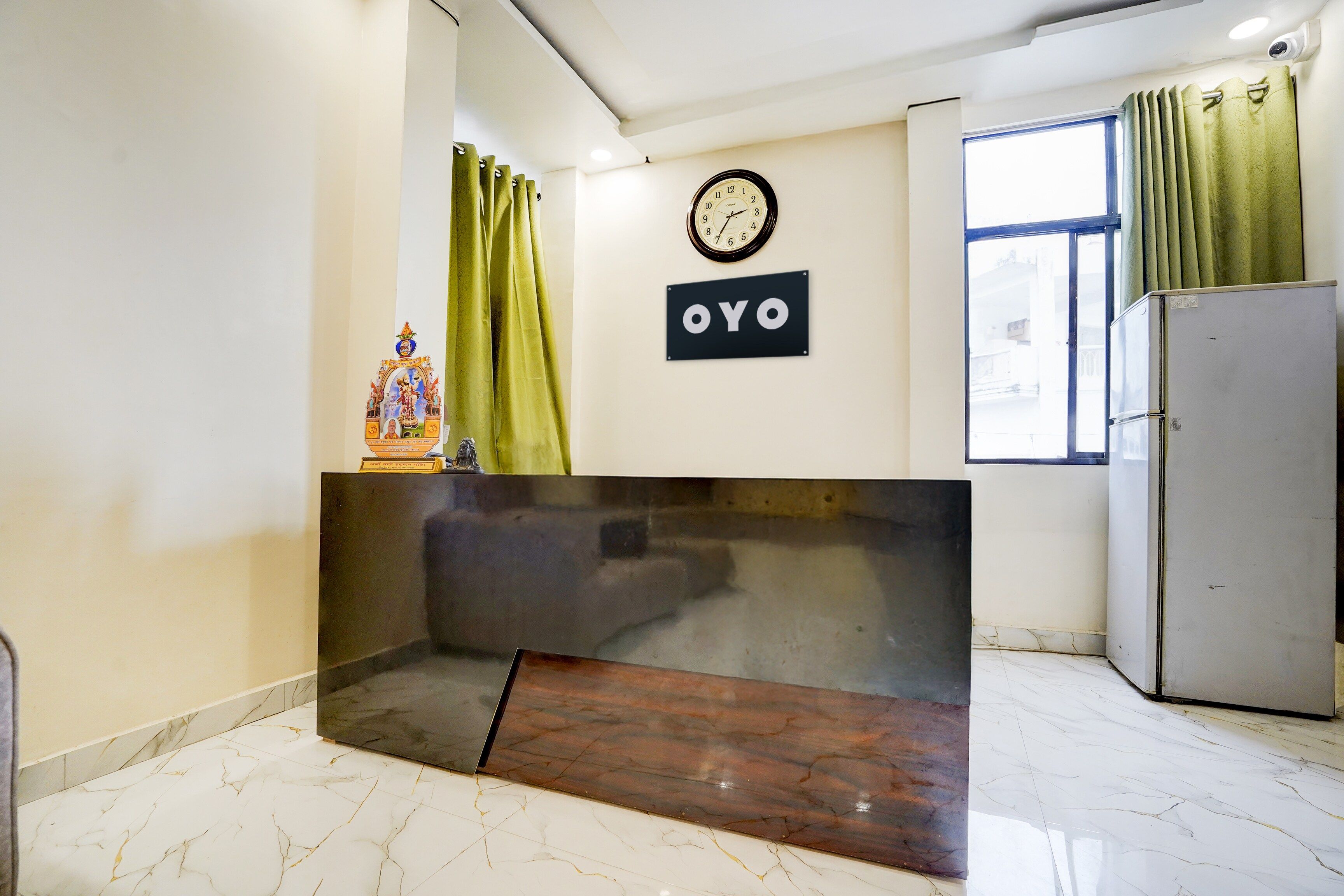 A reception area with a marble floor, a clock, a sign with 'OYO' branding, and a refrigerator.