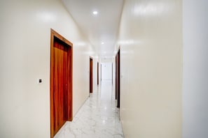 A hallway with white walls and marble flooring, leading to multiple doors. - Hotel O Hotel Madhvam (Prayagraj)