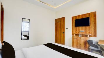 Habitación de hotel con cama, televisor montado en un panel de madera, espejo en la pared y escritorio con silla.