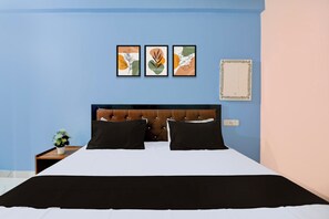A bedroom with a bed, two pillows, a nightstand with a plant, and three framed artworks on the wall. - Hotel O Rahul Inn (Prayagraj)