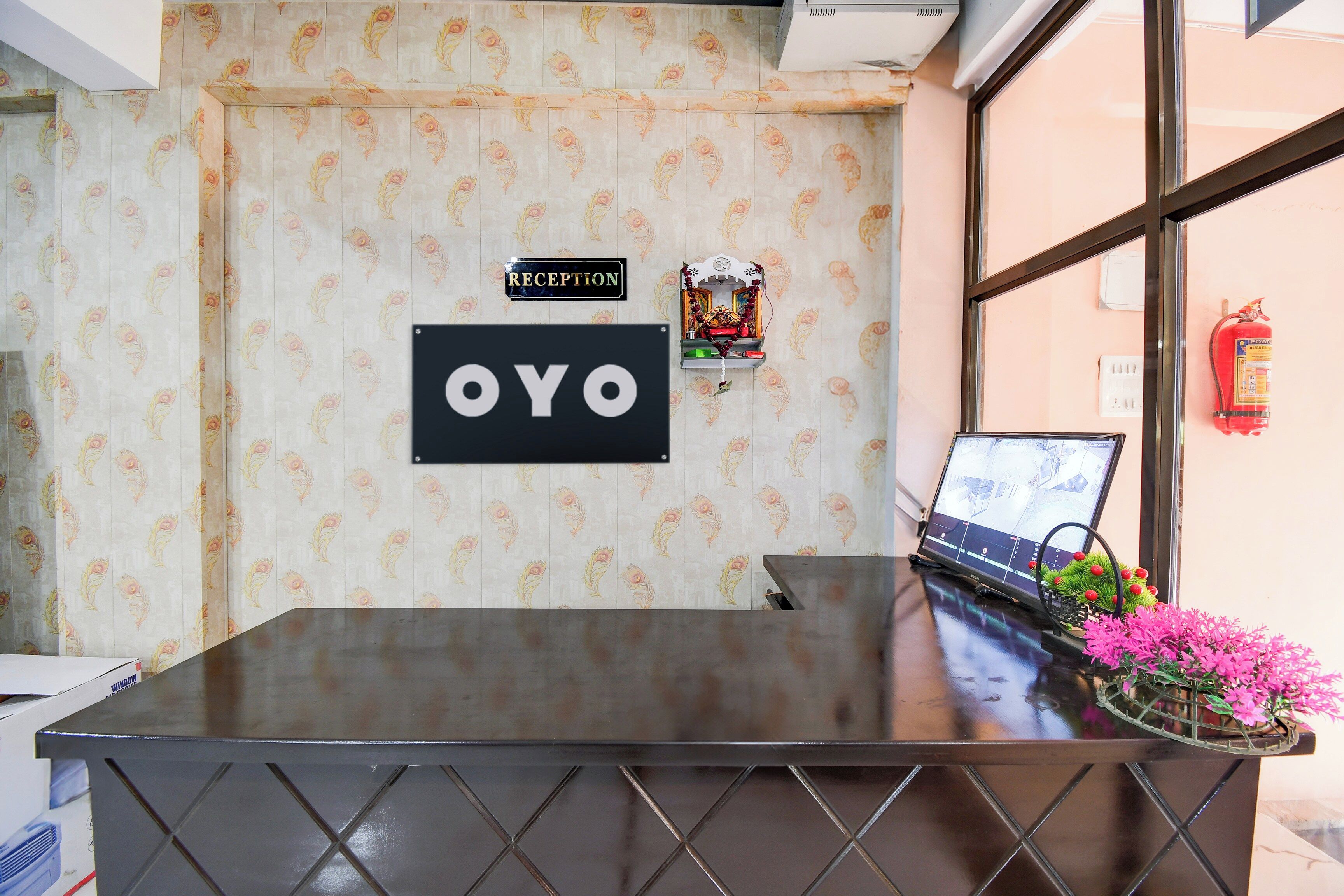 A reception desk with a 'RECEPTION' sign and a 'OYO' sign, a laptop, and a fire extinguisher on the wall.
