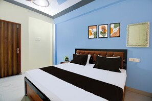 A bedroom with a bed, a nightstand, a wall-mounted power outlet, and a door. - Hotel O Rahul Inn (Prayagraj)