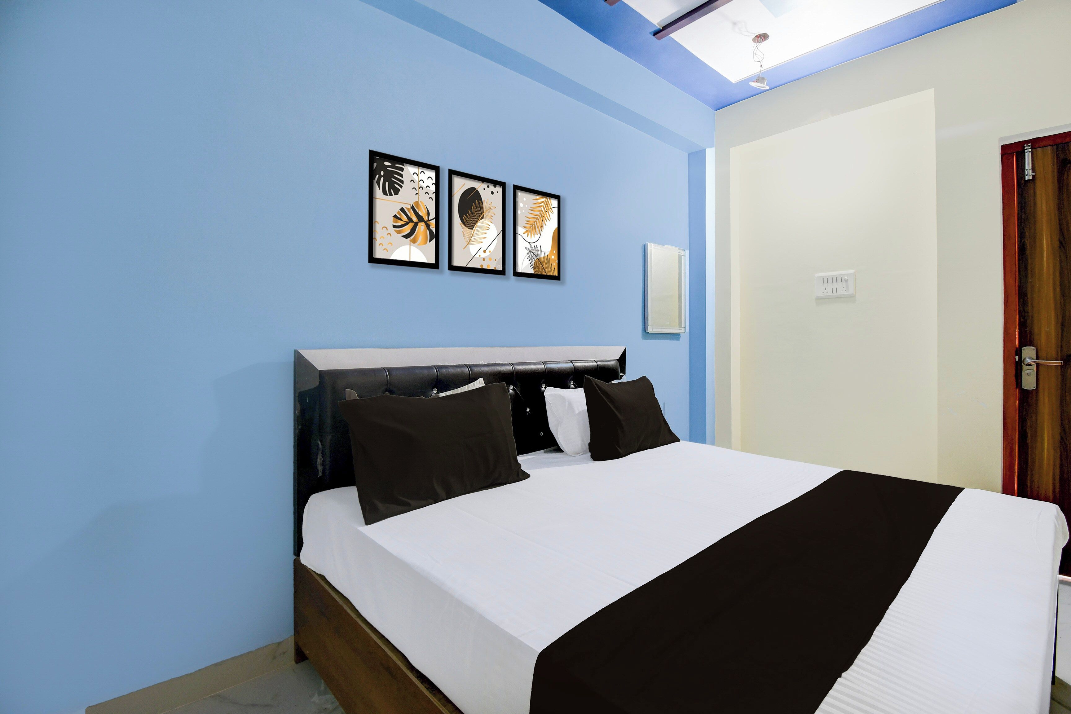 Une chambre à coucher comprenant un lit, une tête de lit, un luminaire fixé au mur et trois œuvres d’art encadrées.