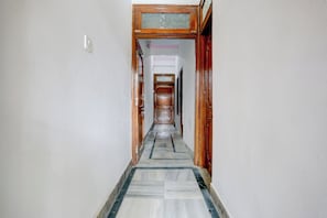 A corridor with a marble floor leading to a room with a wooden door. - Hotel O Lotus Inn (Prayagraj)