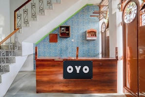 A reception desk with a sign reading 'OYO' in a hotel lobby with a staircase and decorative wall patterns. - Hotel O Lotus Inn (Prayagraj)