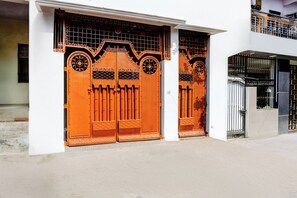 A building with two large orange gates, a white wall, and a metal fence. - Hotel O Lotus Inn (Prayagraj)