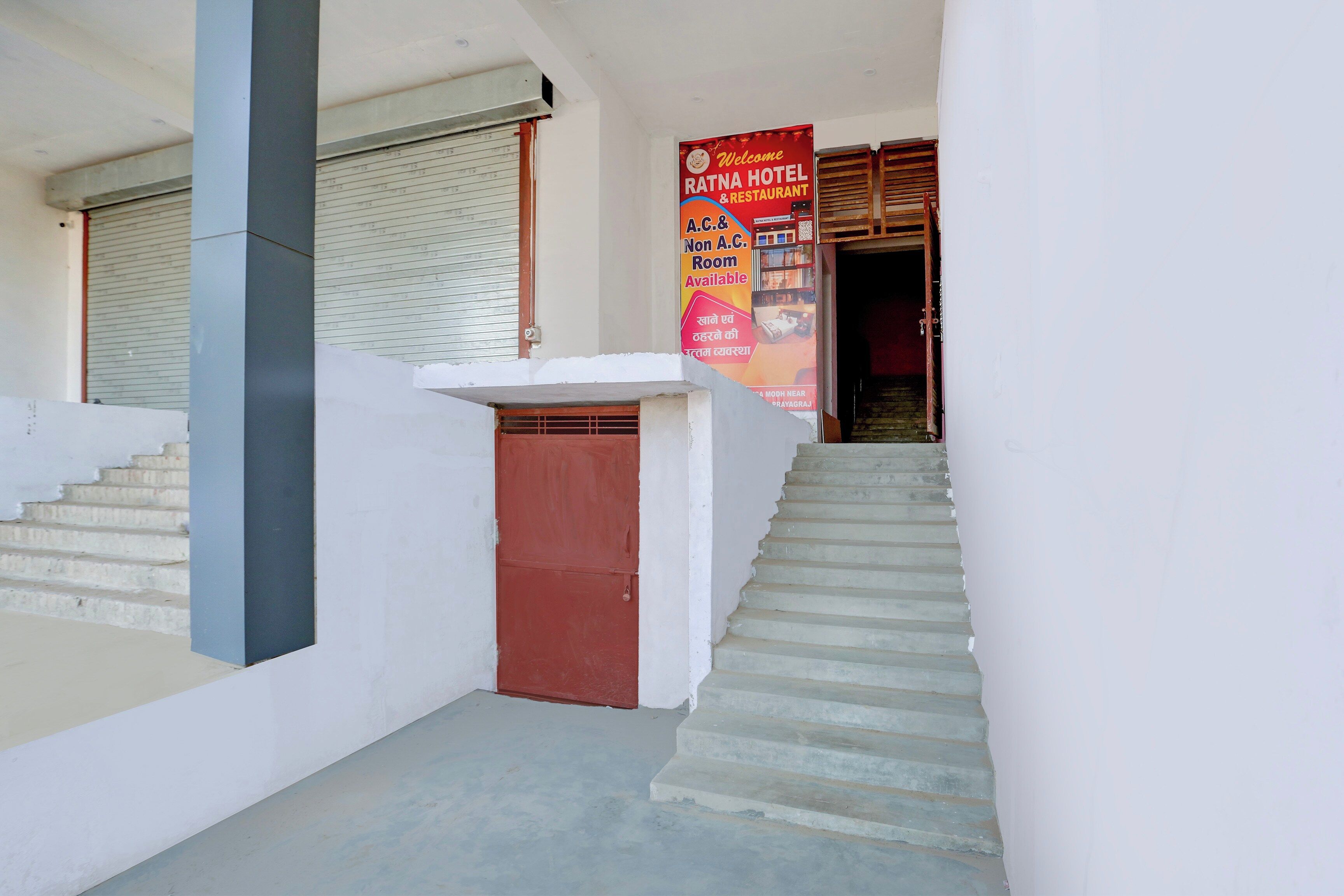Escadaria que leva à entrada de um hotel, com uma porta vermelha e uma placa indicando disponibilidade de quartos com e sem ar condicionado.