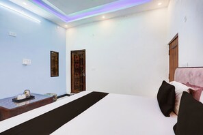 A hotel room with a bed, a bedside table, a mirror, a window with a wooden door, and a wall with a light switch. - Hotel O RATNA HOTEL AND RESTAURANT (Prayagraj)