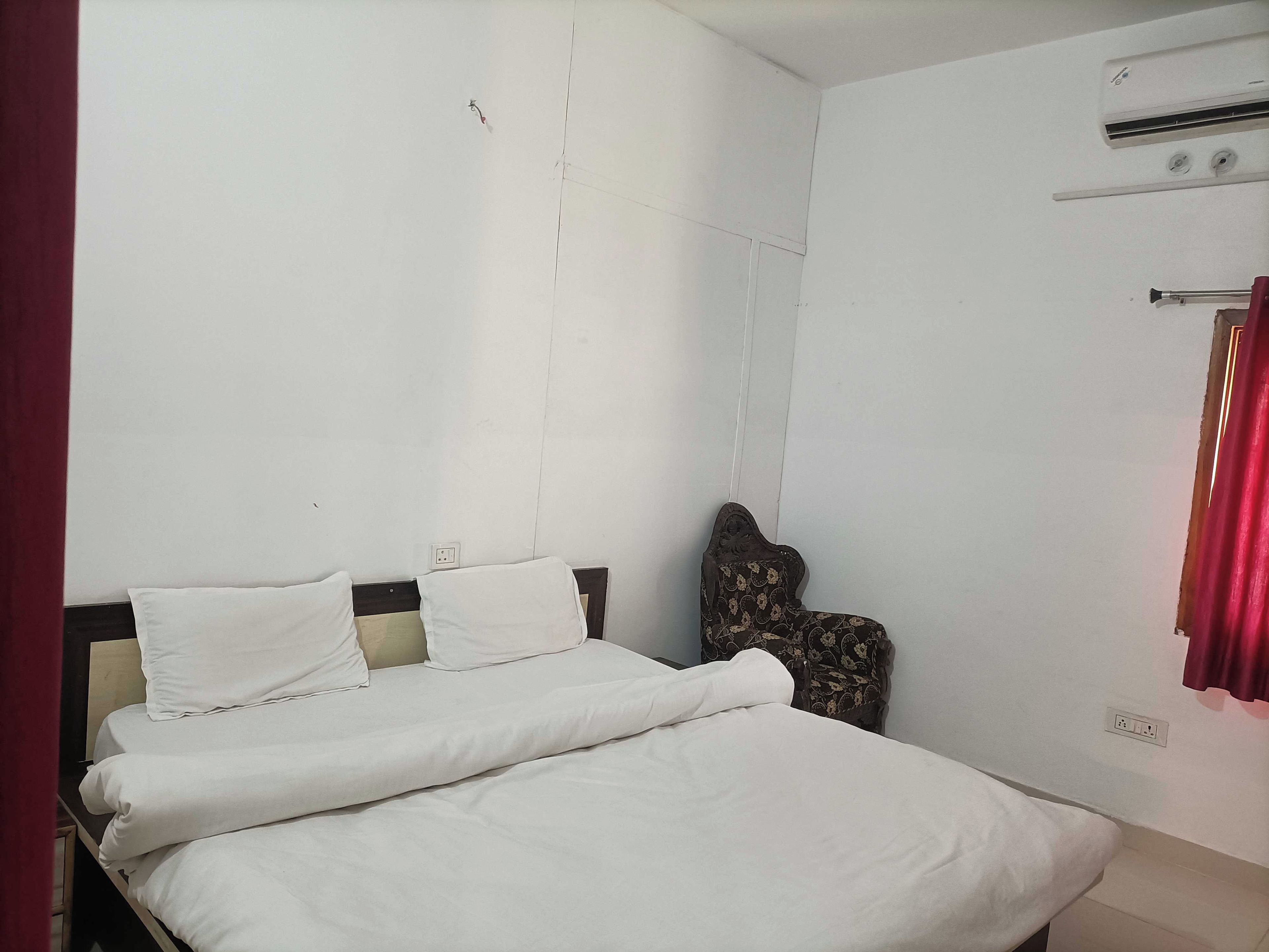 A room with a bed, a chair, a wall socket, and an air conditioning unit.