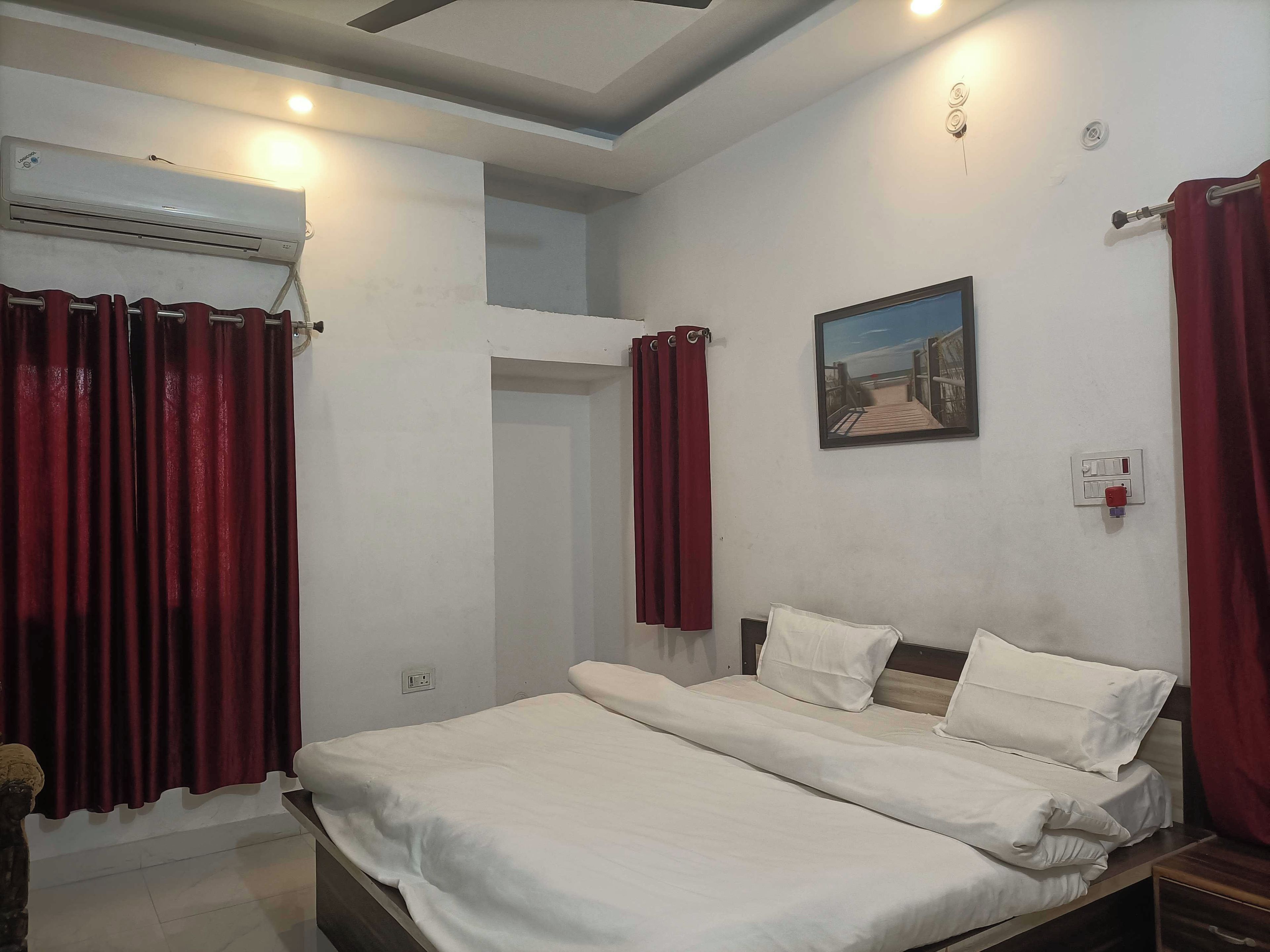 A hotel room with a bed, a painting on the wall, and an air conditioning unit.