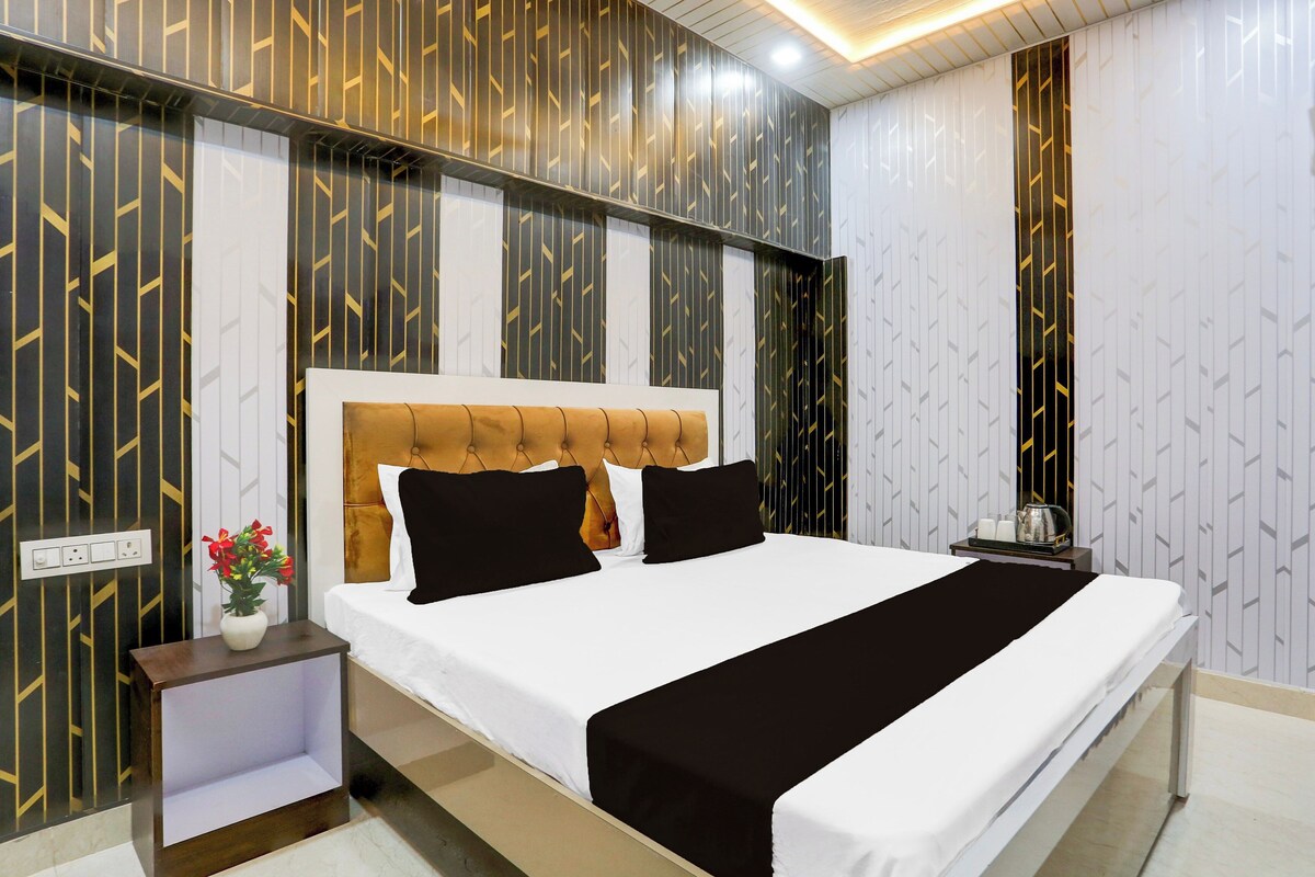 Een hotelkamer met een groot bed, een nachtkastje, een vaas met bloemen en een muur met een geometrisch patroon.