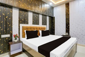 Een hotelkamer met een groot bed, een nachtkastje, een vaas met bloemen en een muur met een geometrisch patroon.