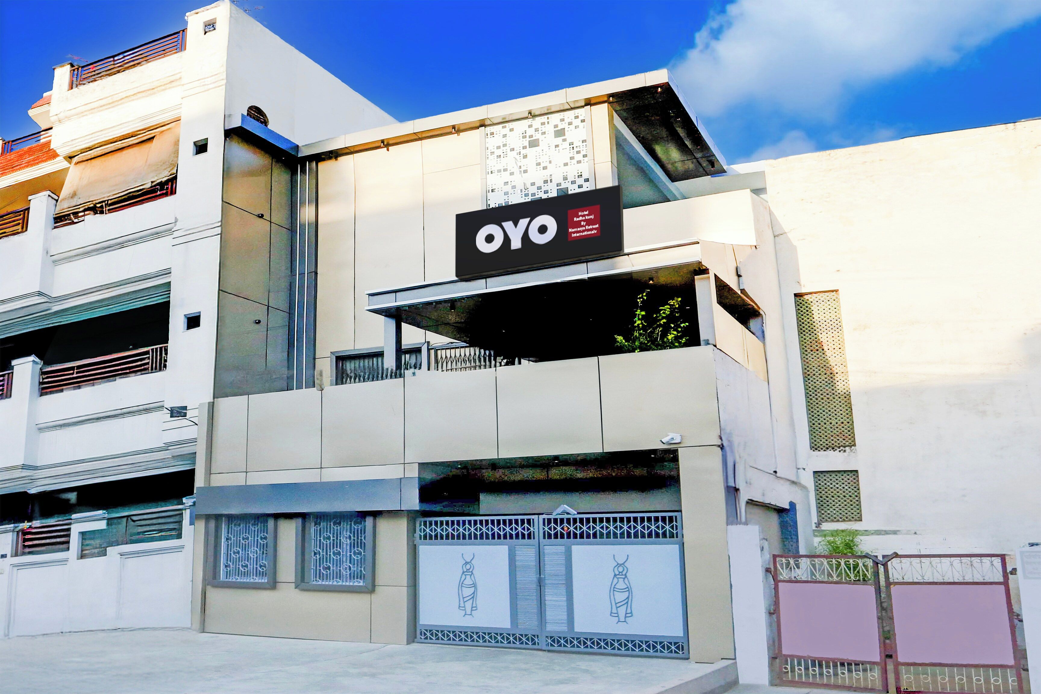 A modern hotel building with a prominent 'OYO' sign, a gated entrance, and a balcony with railings.