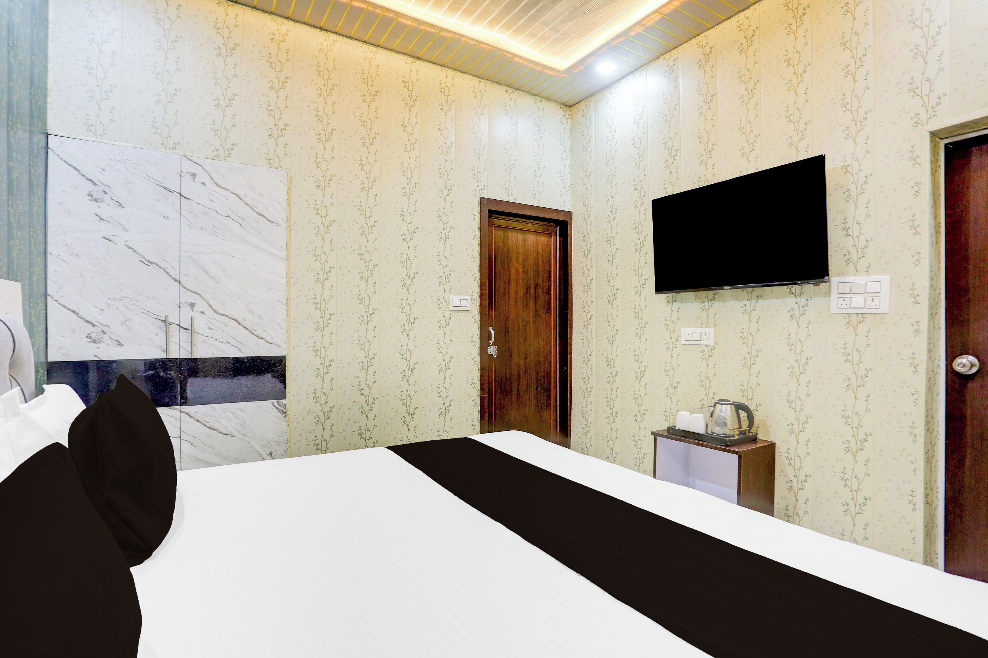 A hotel room with a bed, a television mounted on the wall, a wooden door, and a small table with a kettle.