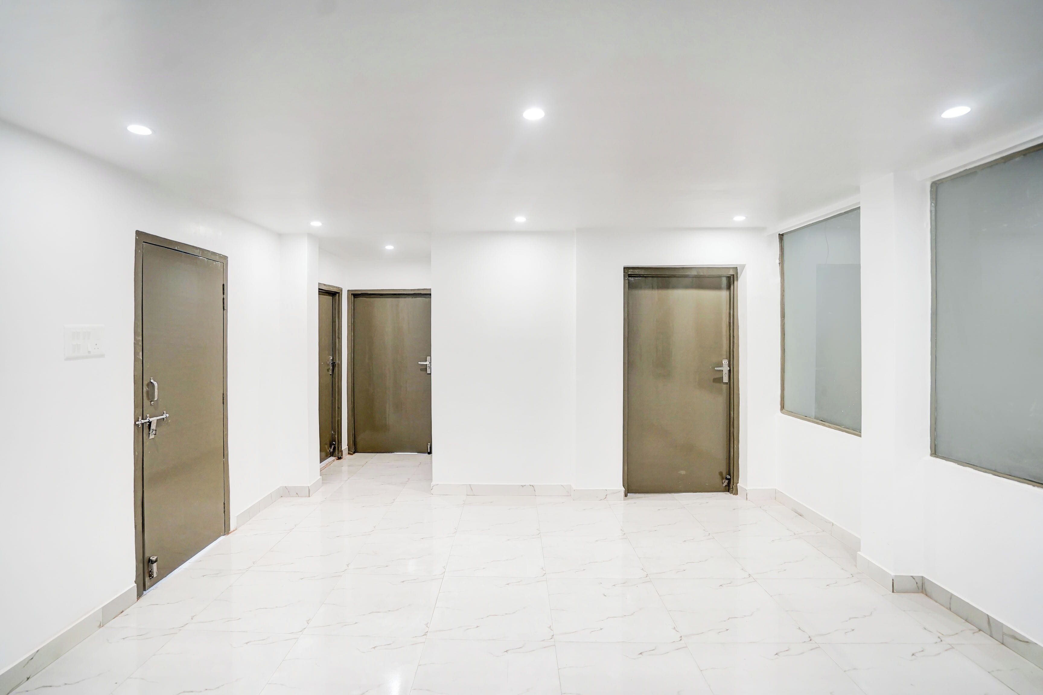 Un pasillo con piso de mármol blanco, tres puertas y un ventanal grande a la derecha.