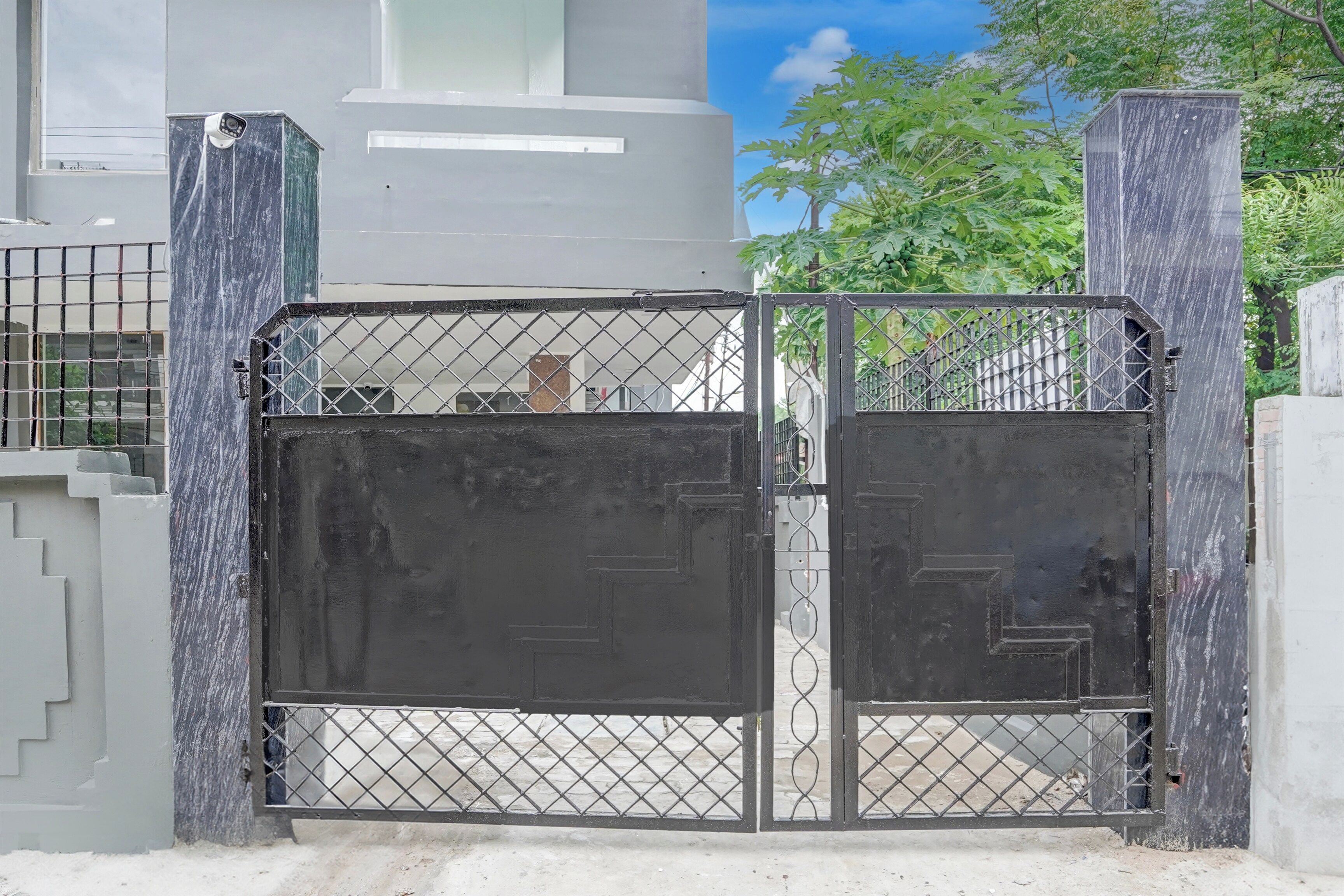 A gated entrance with a metal gate and a concrete pathway leading to a building.
