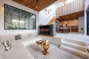 A modern living space with a large window, a Netflix logo, a staircase, and a kitchen area. - 2BR Private Pool Villa with Rice Field Views & Sunset Balconies (Badung)