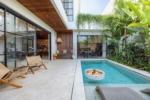 A modern outdoor pool area with lounge chairs, a dining area, and a view of the surrounding greenery. - 2BR Private Pool Villa with Rice Field Views & Sunset Balconies (Badung)