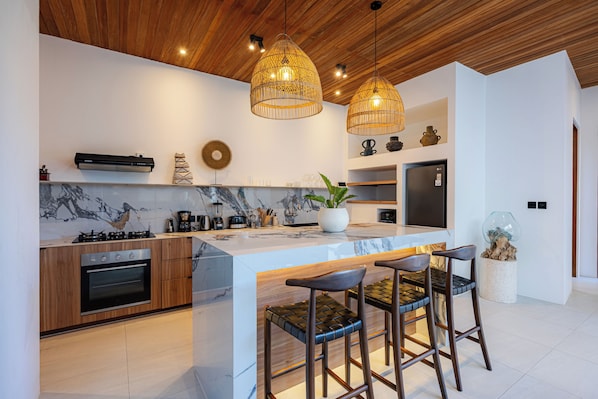A modern kitchen with a central island, bar stools, a built-in oven, and a coffee machine. - 2BR Private Pool Villa with Rice Field Views & Sunset Balconies (Badung)