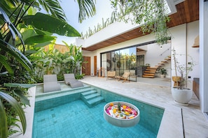 A modern outdoor pool area with a glass door leading to a living space, surrounded by lush greenery. - 2BR Private Pool Villa with Rice Field Views & Sunset Balconies (Badung)