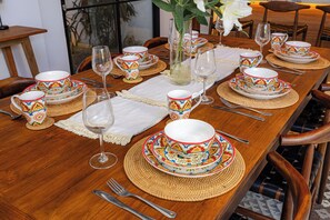 Een eettafel gedekt met kleurrijk servies, helder glaswerk en geweven tafelonderzetters.